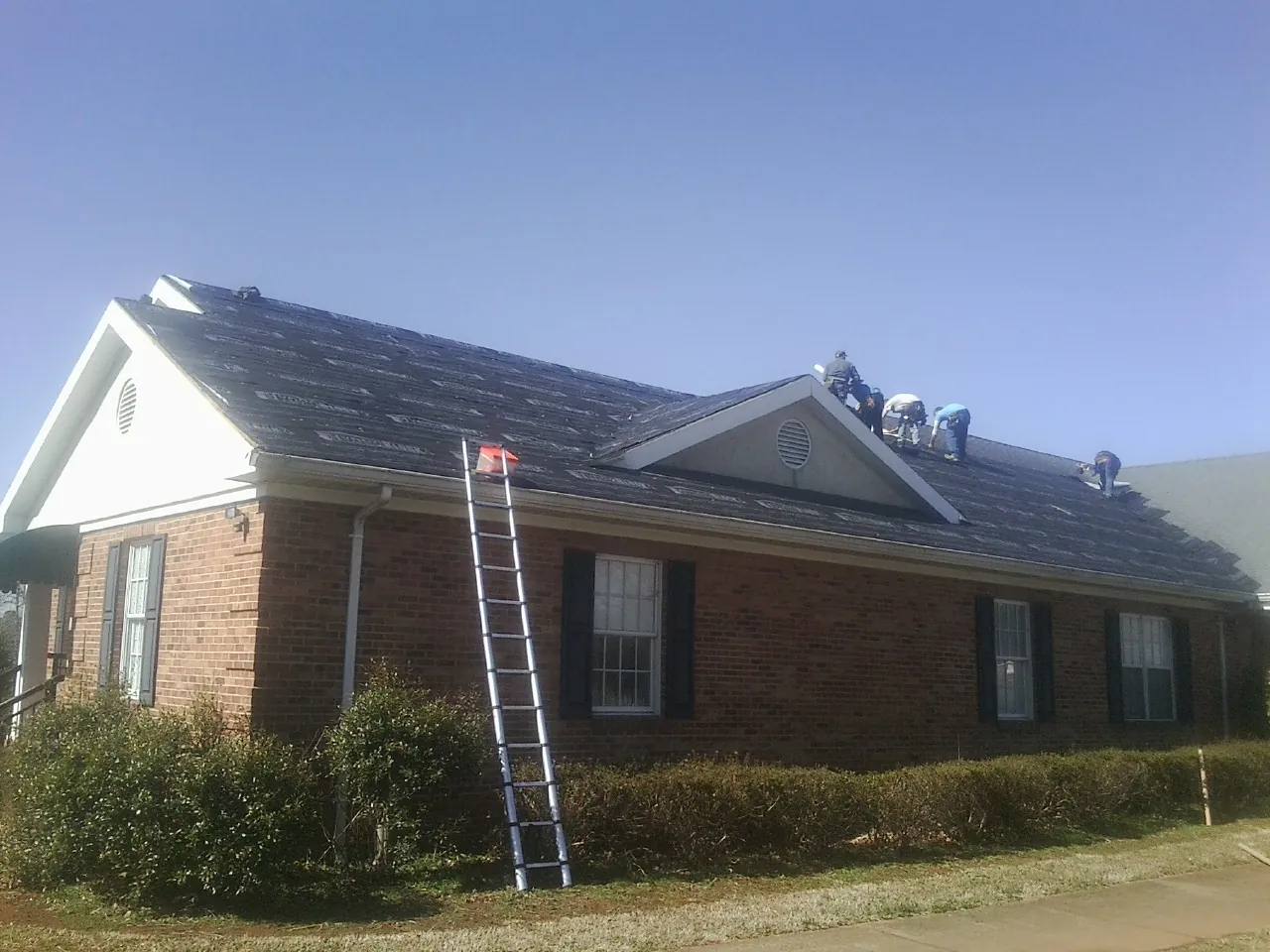 Crew tearing shingles off a brick ranch roof with a ladder set — Emergency Roof Repair work by our crew in Wabasha