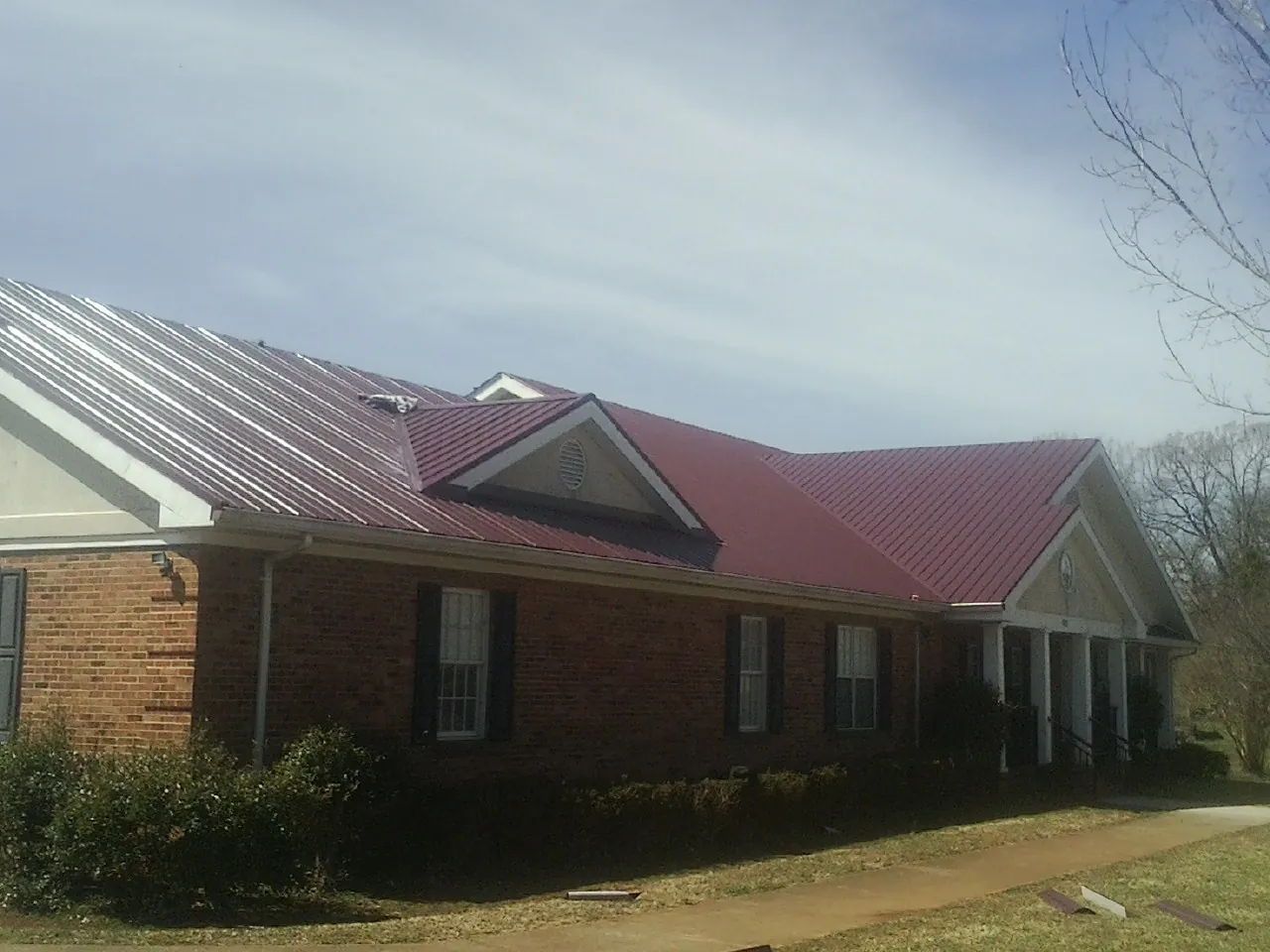 Red metal roof with gabled entries on a long brick building, from a Hail Damage Roof Repair job in Wabasha
