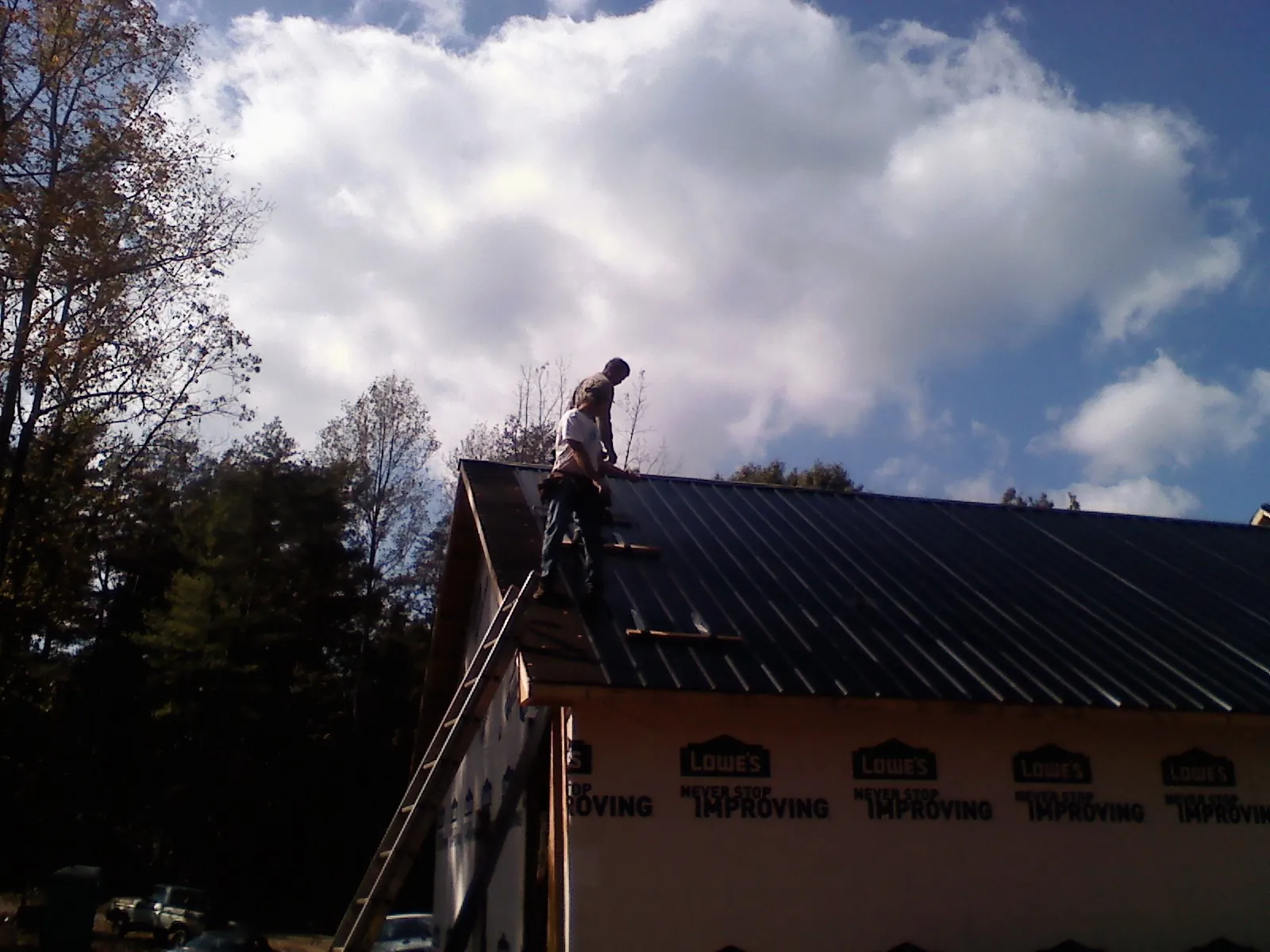 Roofer fastening dark metal panels high against a cloudy sky, from a Roof Inspection job in Wabasha