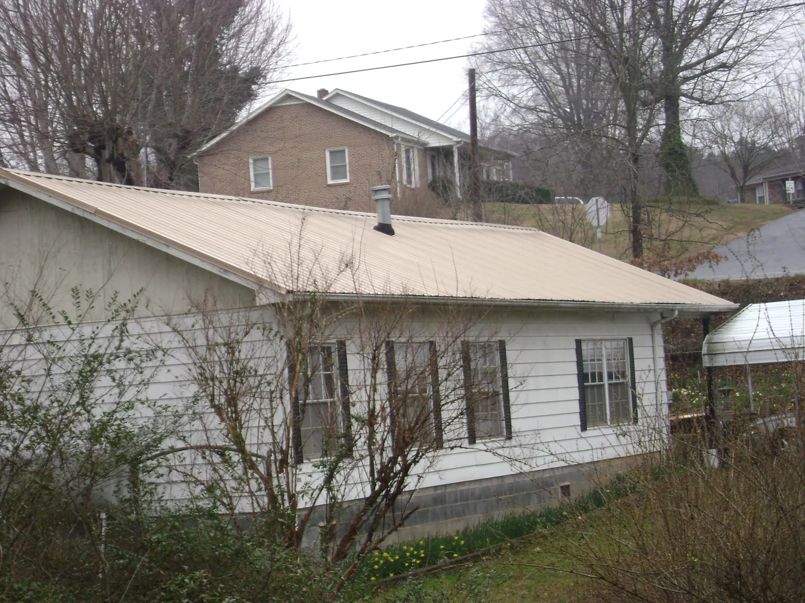 Tan metal roof on a white sided house set into a hillside — Commercial Roofing by Roofing Brothers in Wabasha