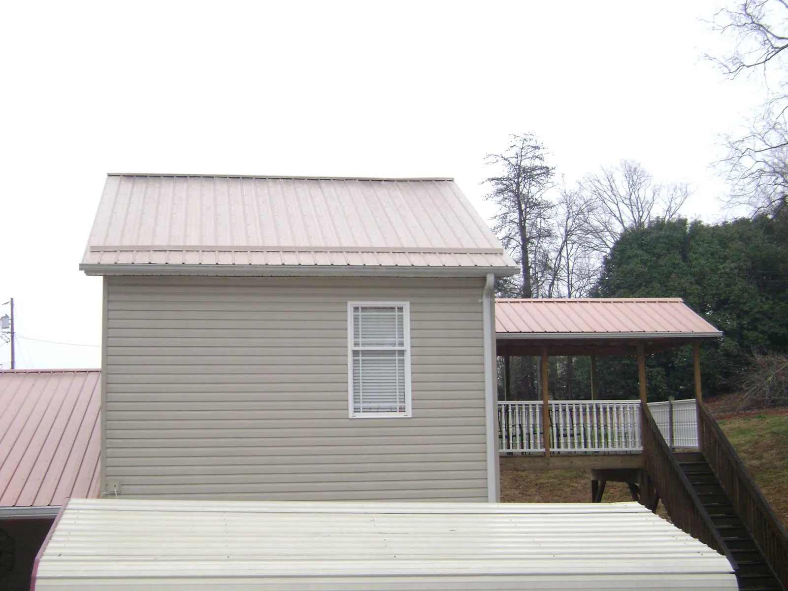 Tan metal roofs on a two story addition and attached porch, from a Roof Replacement job in Wabasha
